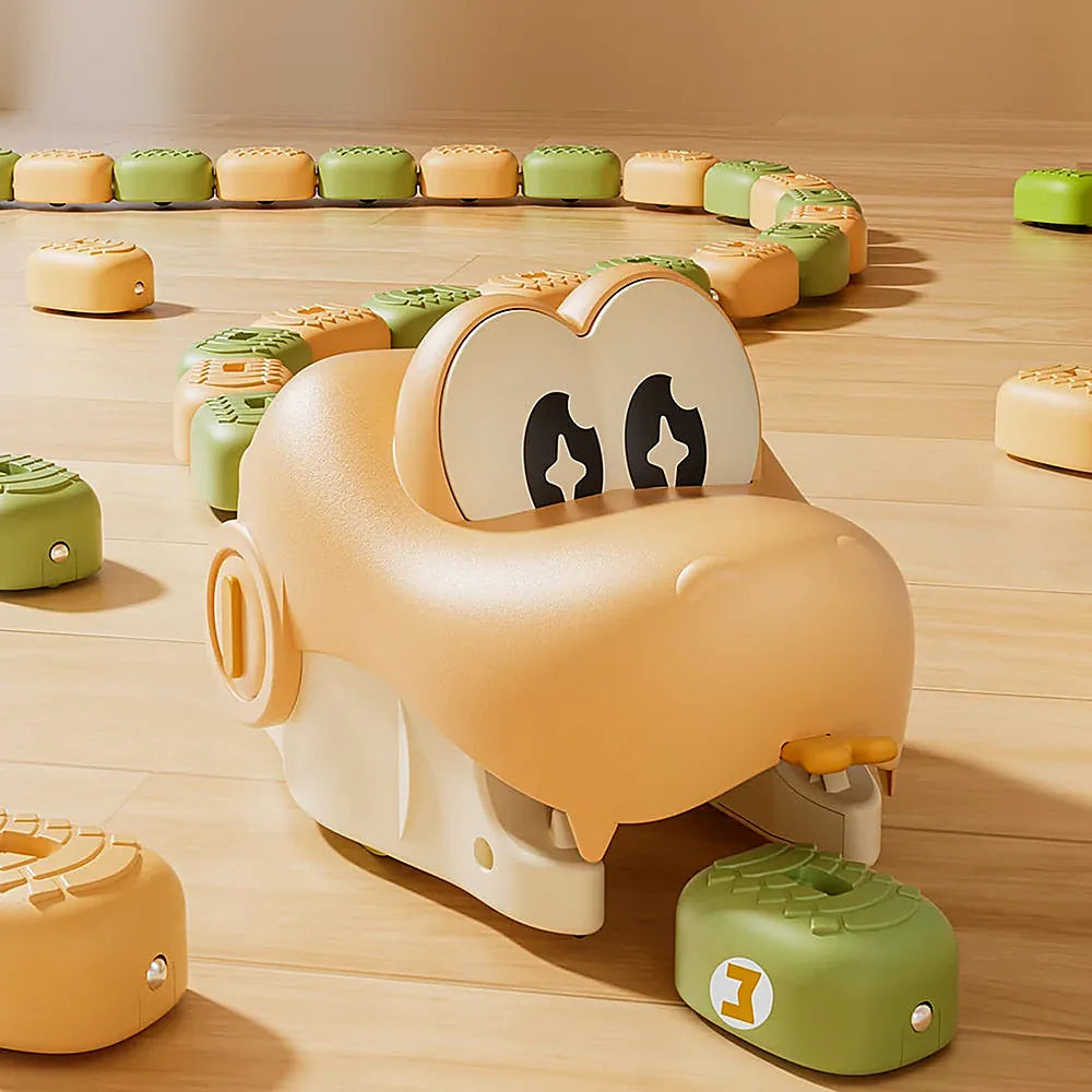 A playful toy setup on a light wood floor featuring a large beige snake shaped vehicle with cartoon eyes, surrounded by small round toy pieces in beige and green arranged in a curved path.