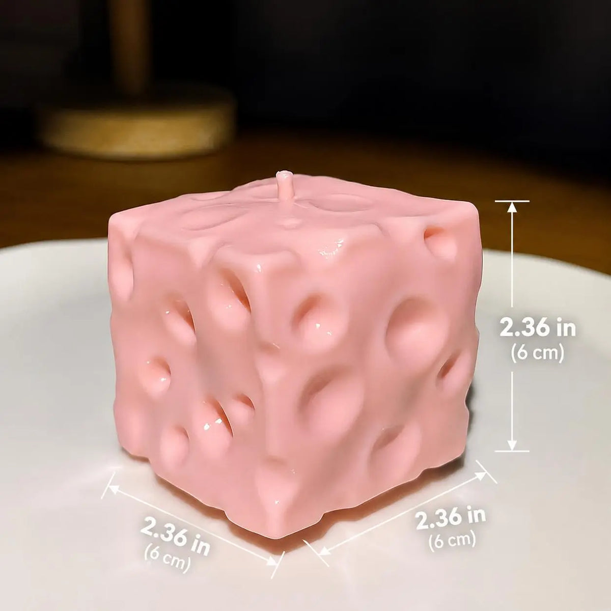 A pink Moldable Cheese Squishy with a textured, pitted surface resembling cheese, shown on a white plate with overlaid dimension lines and text indicating a height and two side lengths of 2.36 in (6 cm).