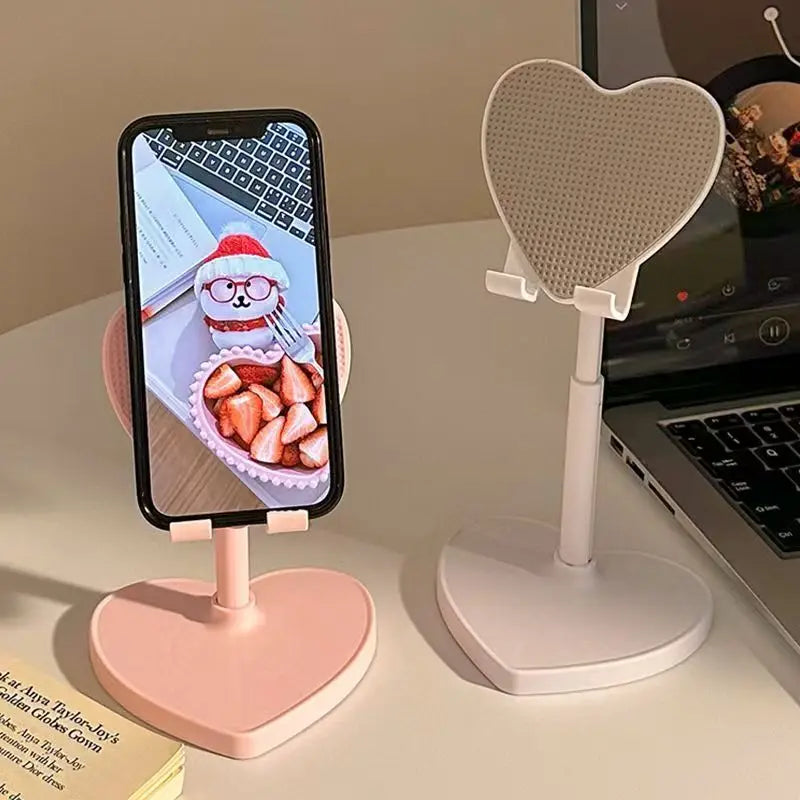 Heart-shaped phone stands on a desk with a smartphone displaying an image of a cartoon character.
