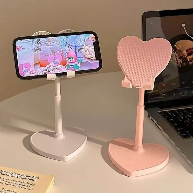 Heart-shaped phone stands on a desk with a smartphone and laptop in the background.