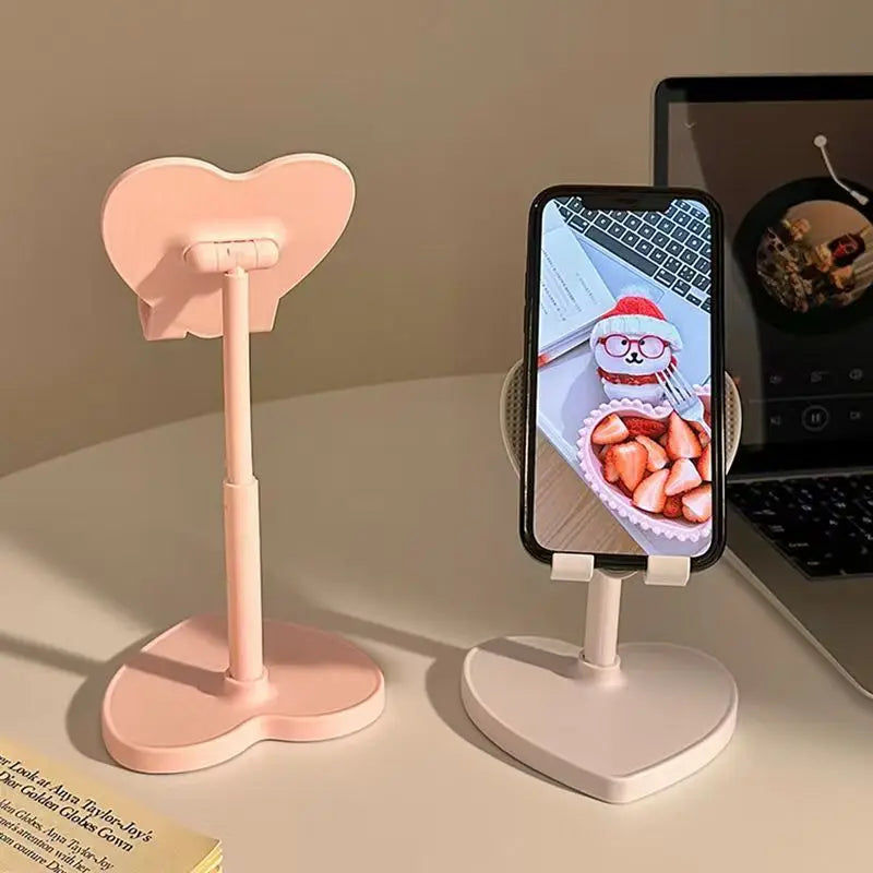 Heart-shaped phone stands on a desk with a phone displaying a cartoon character.