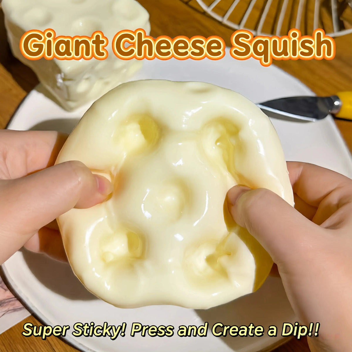 Hands holding a large, pale yellow, sticky cheese-like squishy toy with recessed holes, with text overlays reading 'Giant Cheese Squish' and 'Super Sticky! Press and Create a Dip!!'.